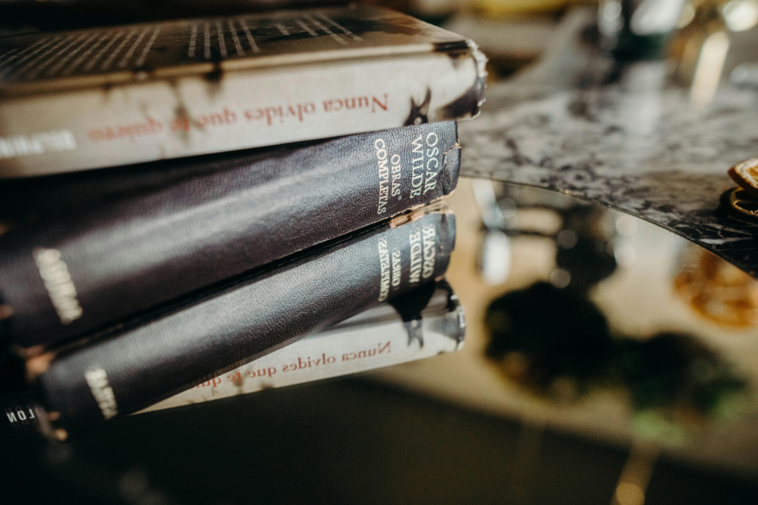 Artistic close-up of stacked books reflecting on a glossy marble surface, indoors.